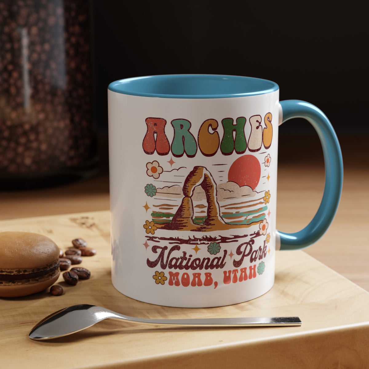 11 oz light blue Arches National Park souvenir mug featuring a scenic design with mountains, arches, and a colorful sunset from Utah.