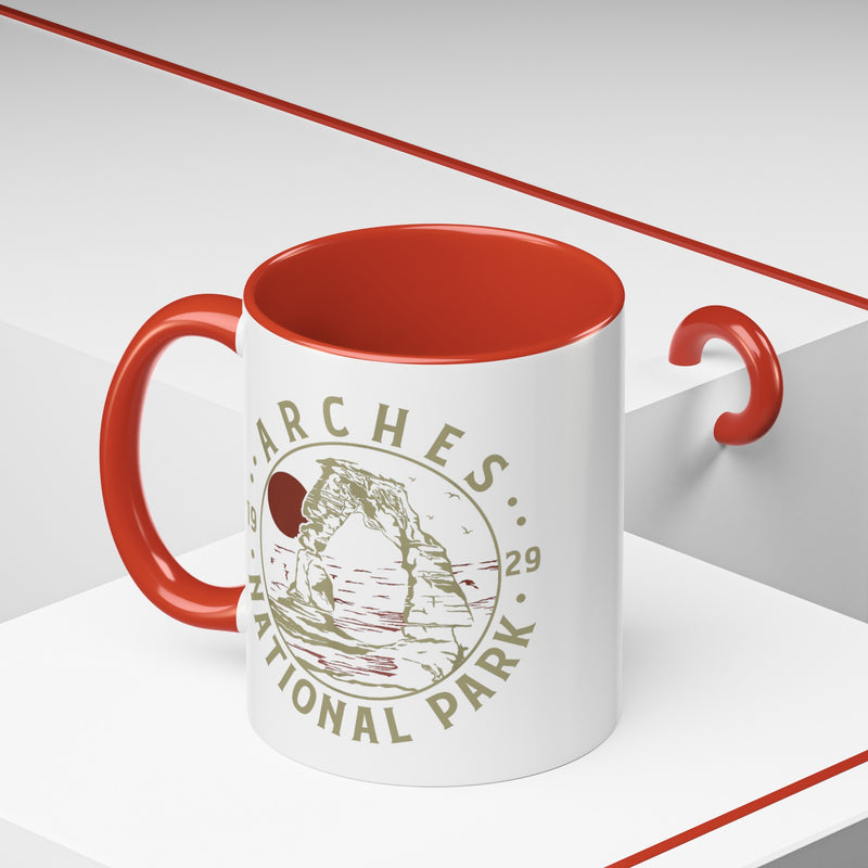 White ceramic mug with a contrasting handle and interior, featuring a design of Arches National Park with Delicate Arch and a sun graphic.