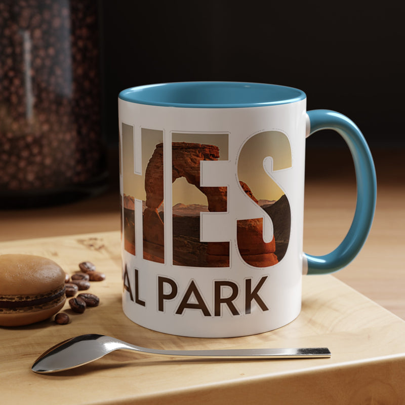 White 11 oz ceramic coffee mug with a light blue handle, featuring a scenic design of Arches National Park, Utah. Perfect for coffee or tea lovers.