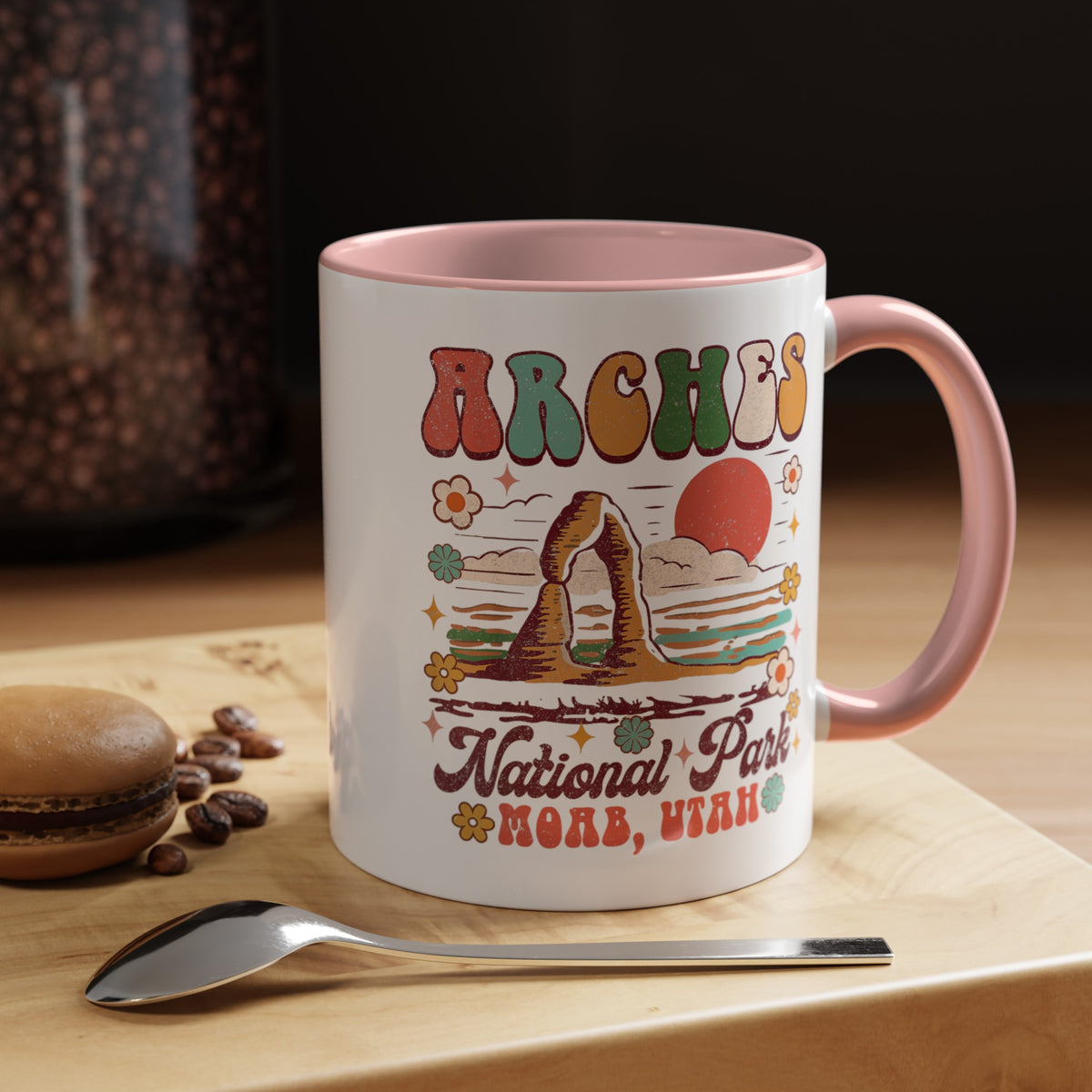 11 oz pink Arches National Park souvenir mug featuring a scenic design with mountains, arches, and a colorful sunset from Utah.