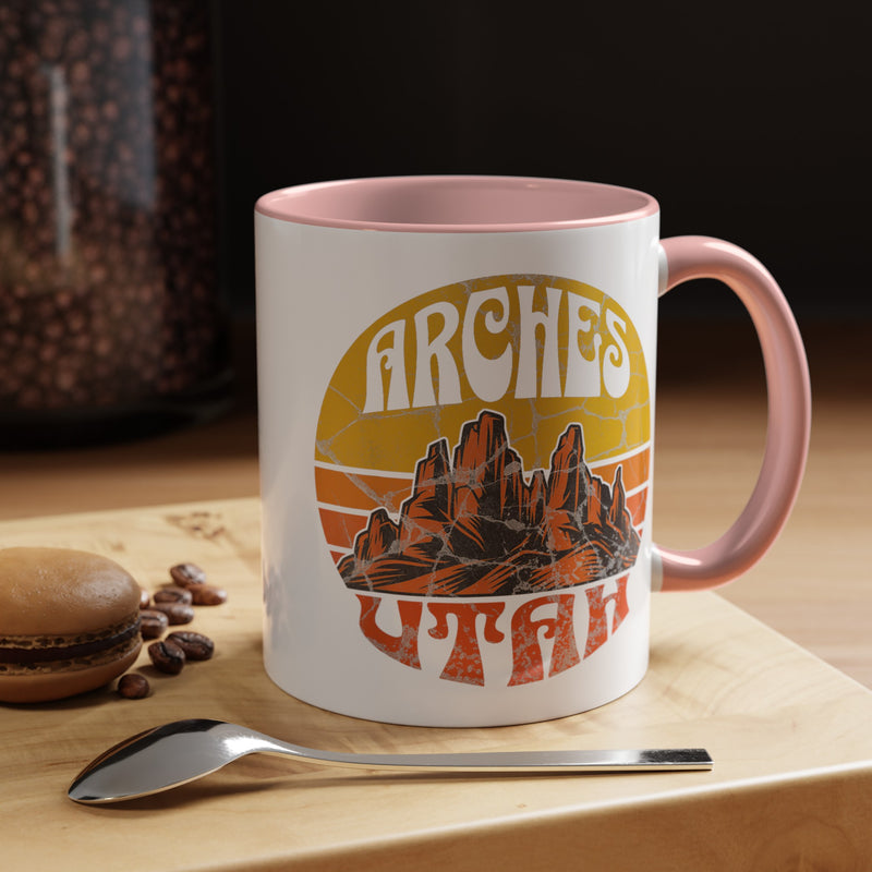 11 oz pink ceramic mug with a contrasting handle and interior, featuring a vibrant design of Arches National Park in Utah, showcasing the park's iconic rock formations.