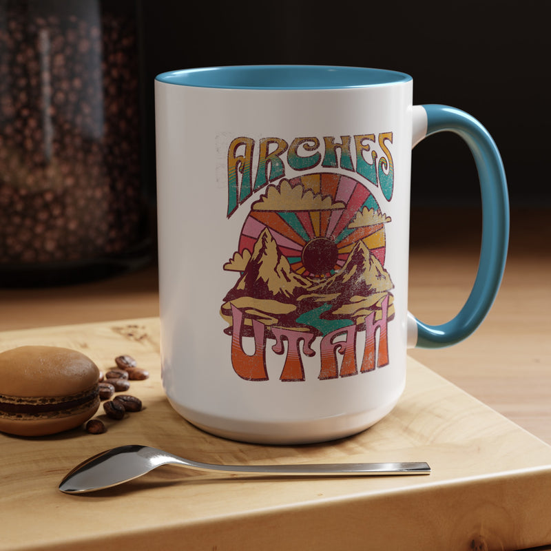 White ceramic mug with a contrasting handle and interior, featuring a colorful scenic design of Arches National Park in Utah.