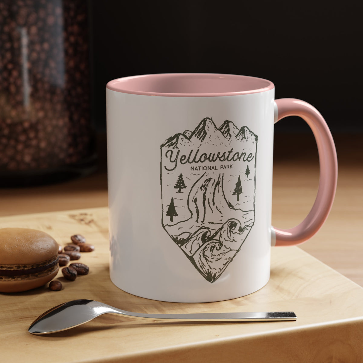 White ceramic mug with a contrasting handle and interior, featuring a minimalist design of Yellowstone National Park with mountains, trees, and a river.