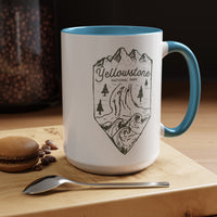 White ceramic mug with a contrasting handle and interior, featuring a minimalist design of Yellowstone National Park with mountains, trees, and a river.