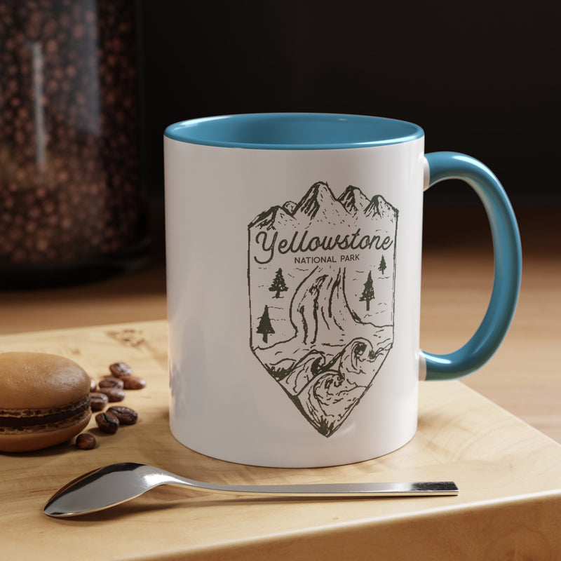 White ceramic mug with a contrasting handle and interior, featuring a minimalist design of Yellowstone National Park with mountains, trees, and a river.