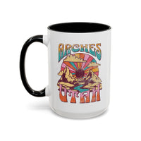 White ceramic mug with a contrasting handle and interior, featuring a colorful scenic design of Arches National Park in Utah.