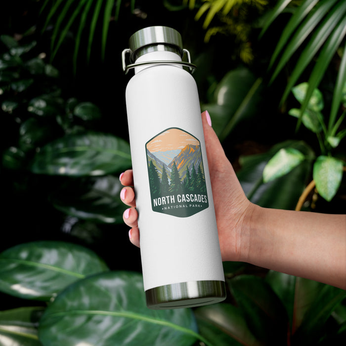 A white double-wall stainless steel water bottle featuring a scenic design inspired by North Cascades National Park, showcasing mountains and pine trees.