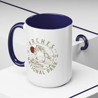 White ceramic mug with a contrasting handle and interior, featuring a design of Arches National Park with Delicate Arch and a sun graphic.