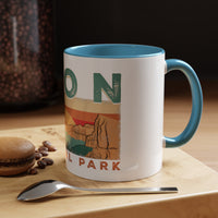 White ceramic mug with contrasting handle and interior, featuring a sunset landscape design of Zion National Park.