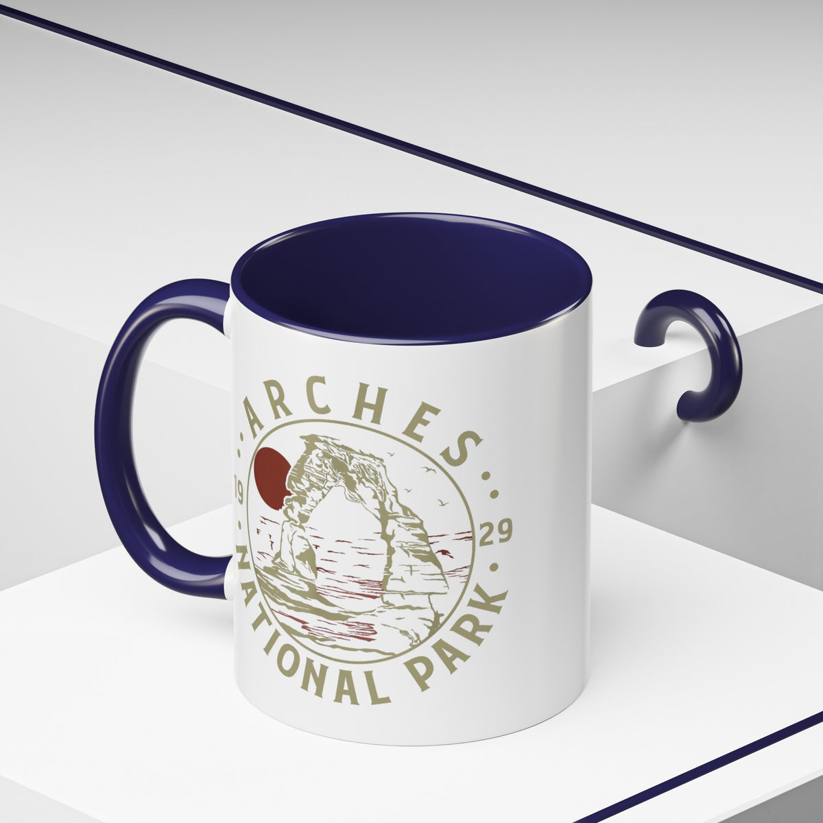 White ceramic mug with a contrasting handle and interior, featuring a design of Arches National Park with Delicate Arch and a sun graphic.