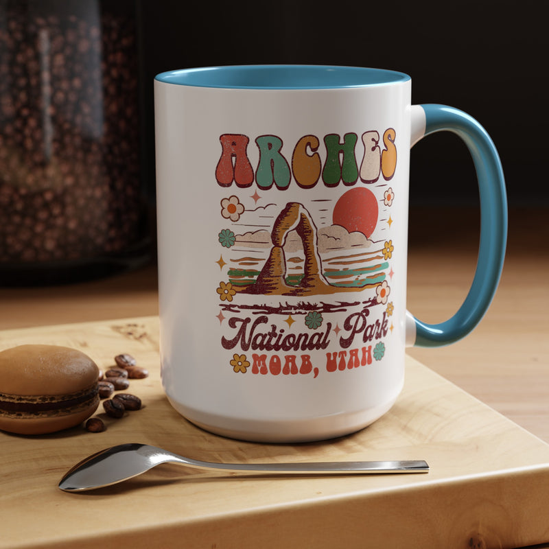 15 oz light blue Arches National Park souvenir mug featuring a scenic design with mountains, arches, and a colorful sunset from Utah.