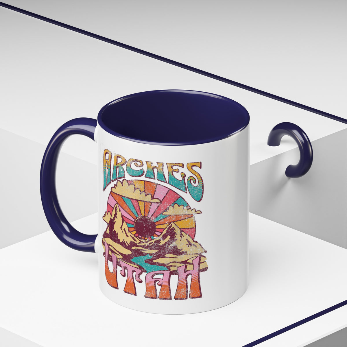 White ceramic mug with a contrasting handle and interior, featuring a colorful scenic design of Arches National Park in Utah.