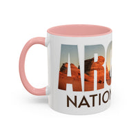 White 11 oz ceramic coffee mug with a pink handle, featuring a scenic design of Arches National Park, Utah. Perfect for coffee or tea lovers.